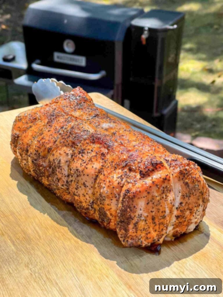 A whole Texas style smoked pork loin resting on a cutting board, recently removed from the smoker.