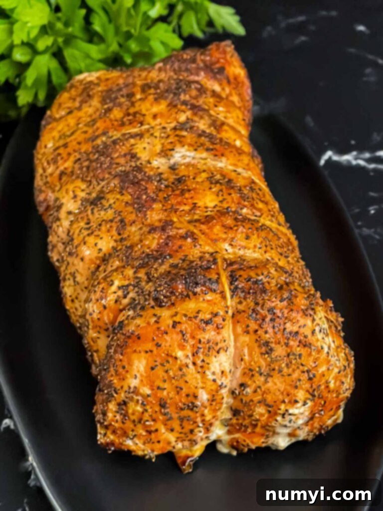 A beautifully smoked Texas style pork loin on a black serving plate, ready to be carved.