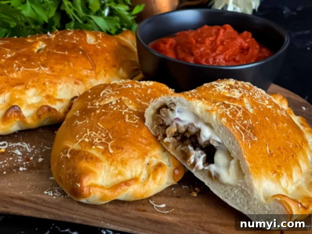 Hearty Italian Sausage Calzone 2 A golden-brown Italian sausage calzone resting on a wooden cutting board, with a small bowl of rich red dipping sauce nearby.