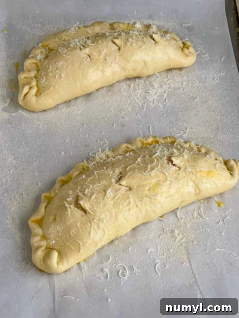 Hearty Italian Sausage Calzone 18 Two unbaked calzones on a parchment-lined baking sheet, brushed with egg wash and ready for the oven, hinting at their future golden crust.