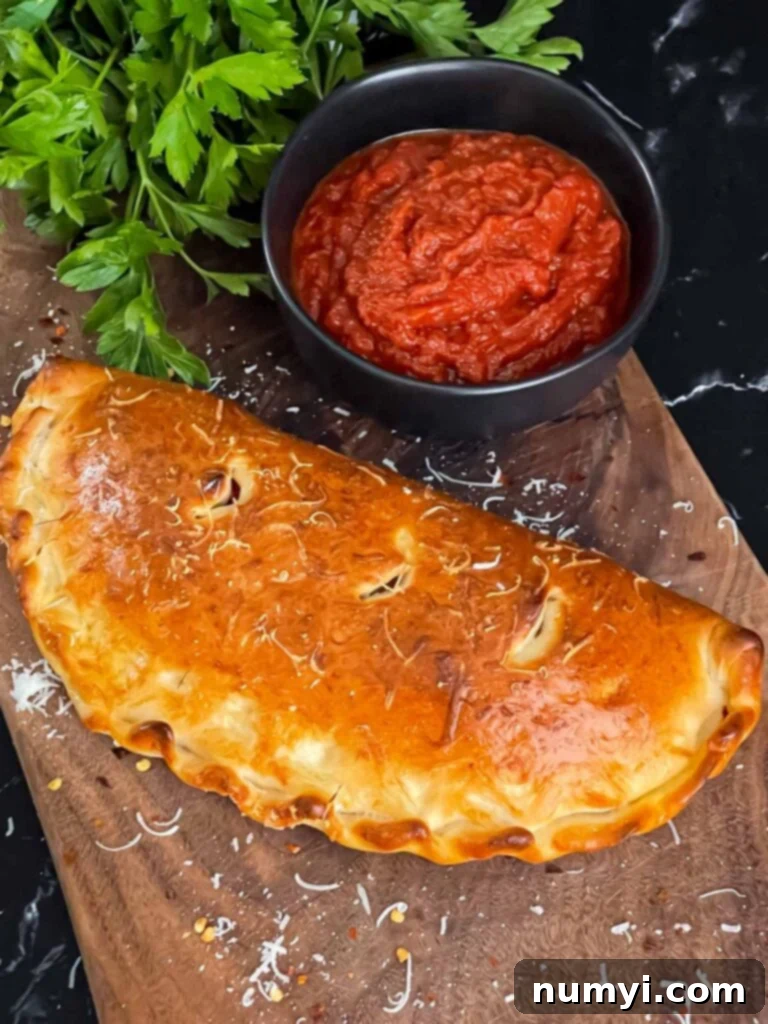 Hearty Italian Sausage Calzone 20 A freshly baked calzone, sliced open on a cutting board, revealing its melted cheese and flavorful sausage filling, with dipping sauce in the background.