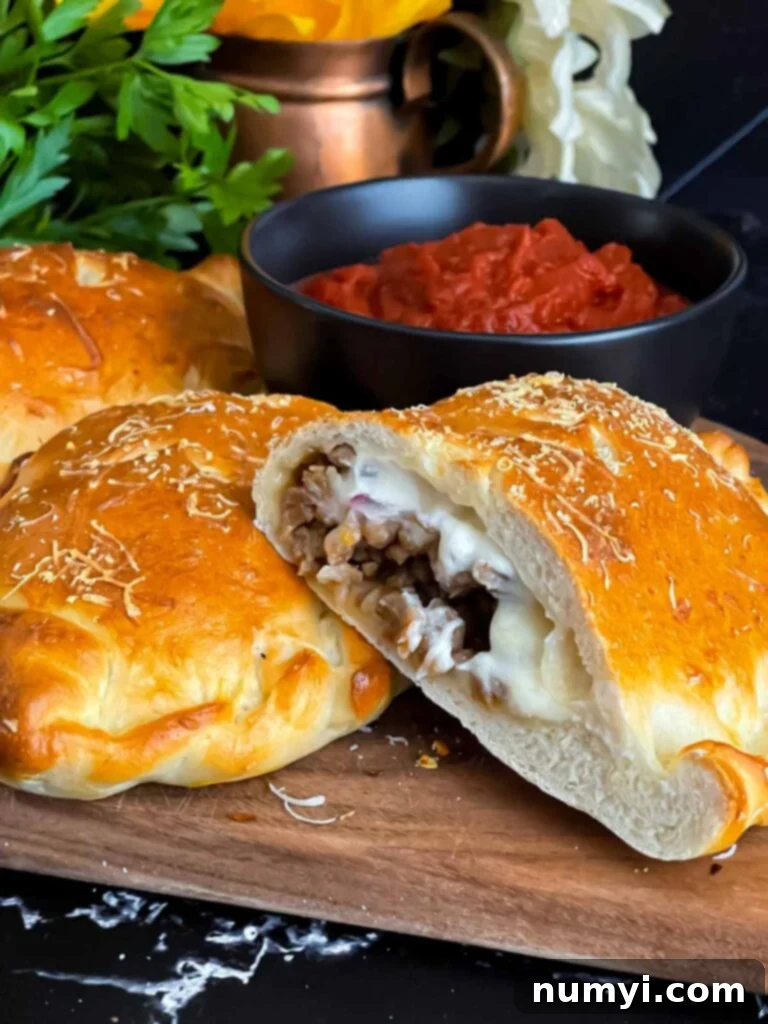 Hearty Italian Sausage Calzone 21 Another view of a delicious calzone on a cutting board, ready to be enjoyed with the accompanying red dipping sauce.