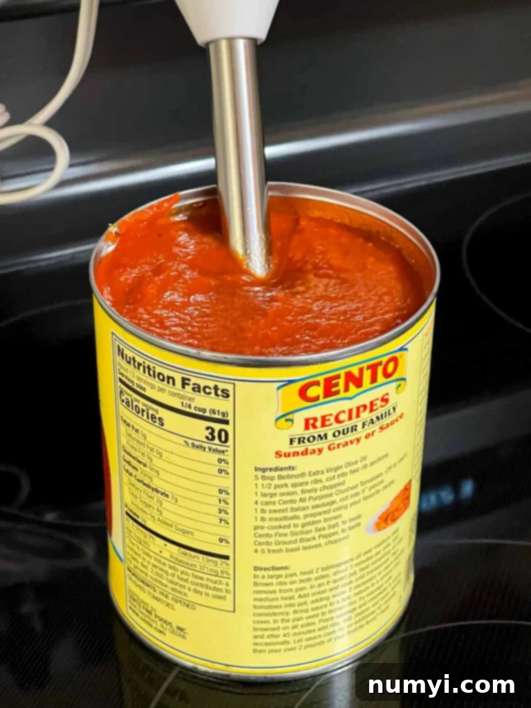 Hearty Italian Sausage Calzone 8 An immersion blender actively blending crushed tomatoes and spices directly in the can, preparing a smooth dipping sauce.