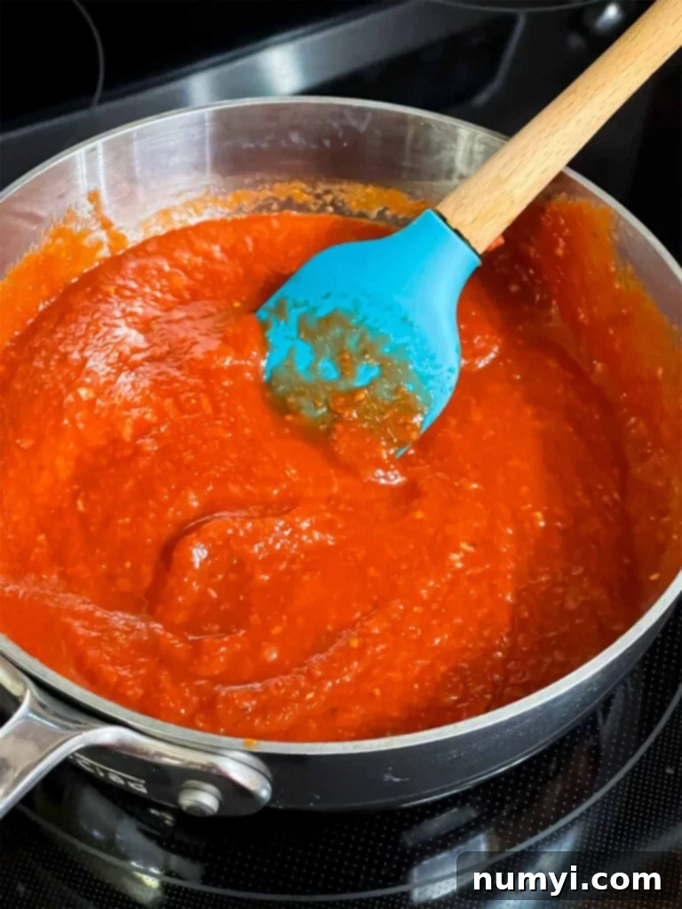 Hearty Italian Sausage Calzone 9 A rich, bubbling calzone dipping sauce simmering in a saucepan on a stovetop, demonstrating its thickening process.
