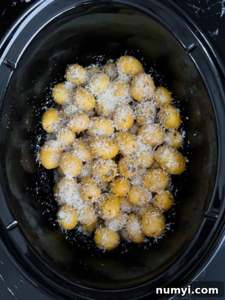 Ultimate Slow Cooker Garlic Parmesan Potatoes 5 Shredded parmesan sprinkled over the seasoned potatoes in the crock of a slow cooker.
