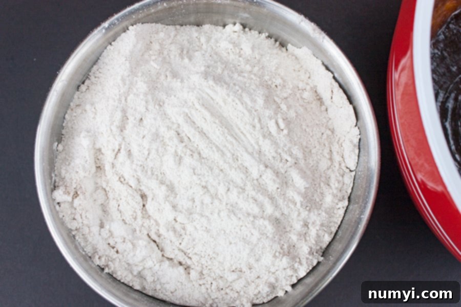Dry ingredients for molasses cookies, including flour, cloves, ginger, cinnamon, baking soda, and salt, mixed together in a metal bowl.