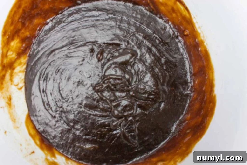 Wet ingredients for molasses cookies, including sugar, molasses, eggs, and cooled melted shortening, mixed together in a white bowl.