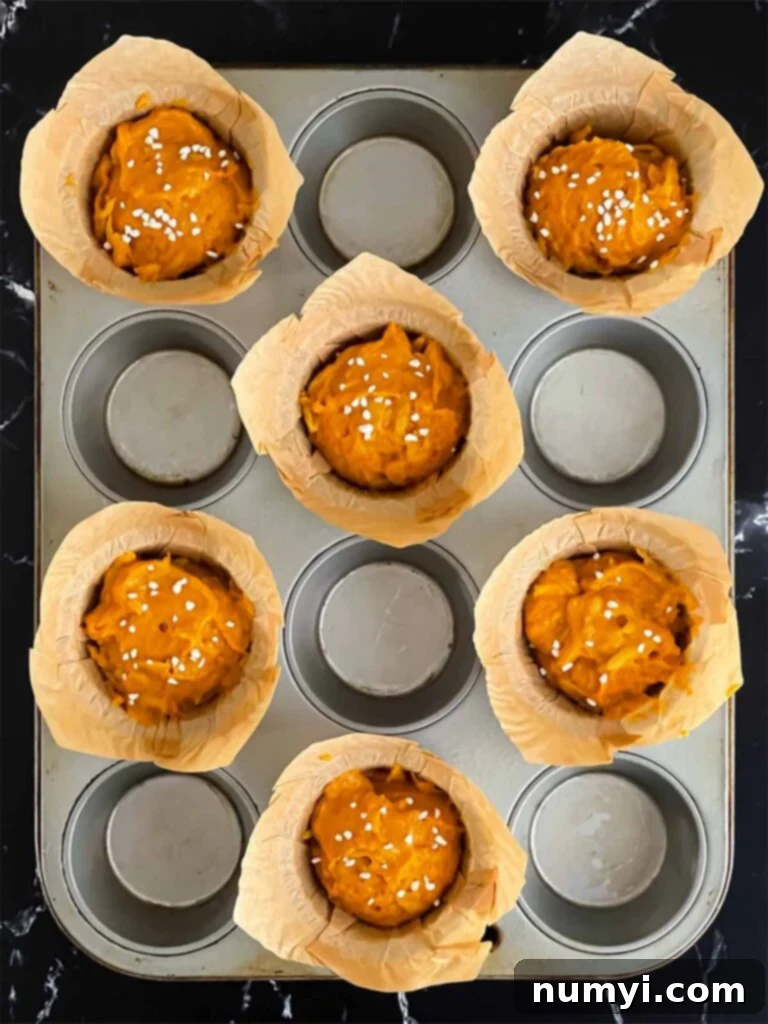 Pumpkin apple muffin batter divided into paper-lined muffin cups, ready for baking, with a sprinkle of pearl sugar on top.