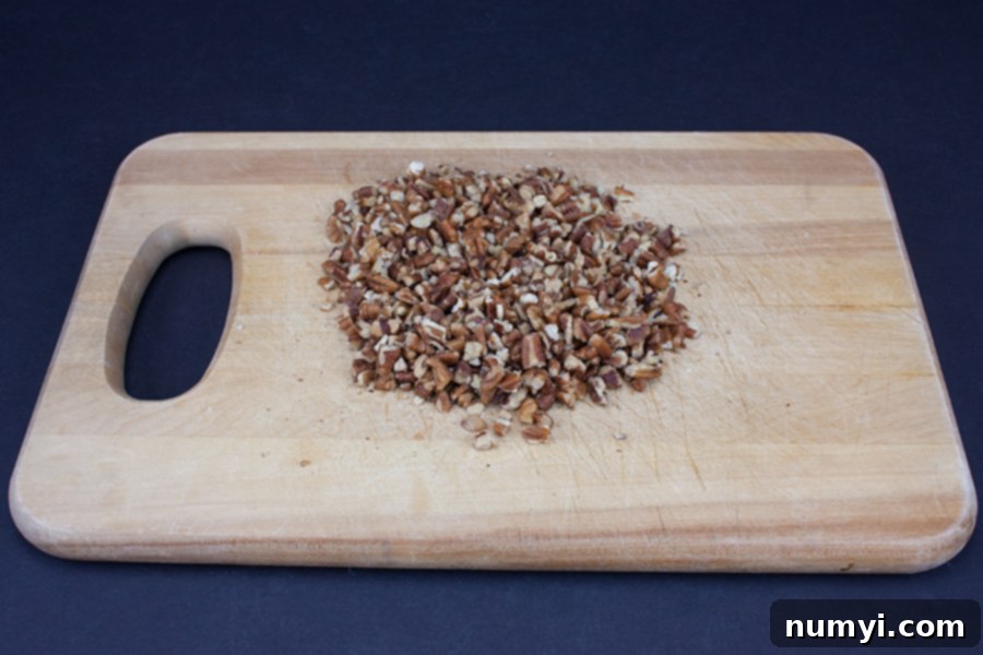 Finely chopped pecans on a wooden cutting board, ready for Italian Butterball Cookies.