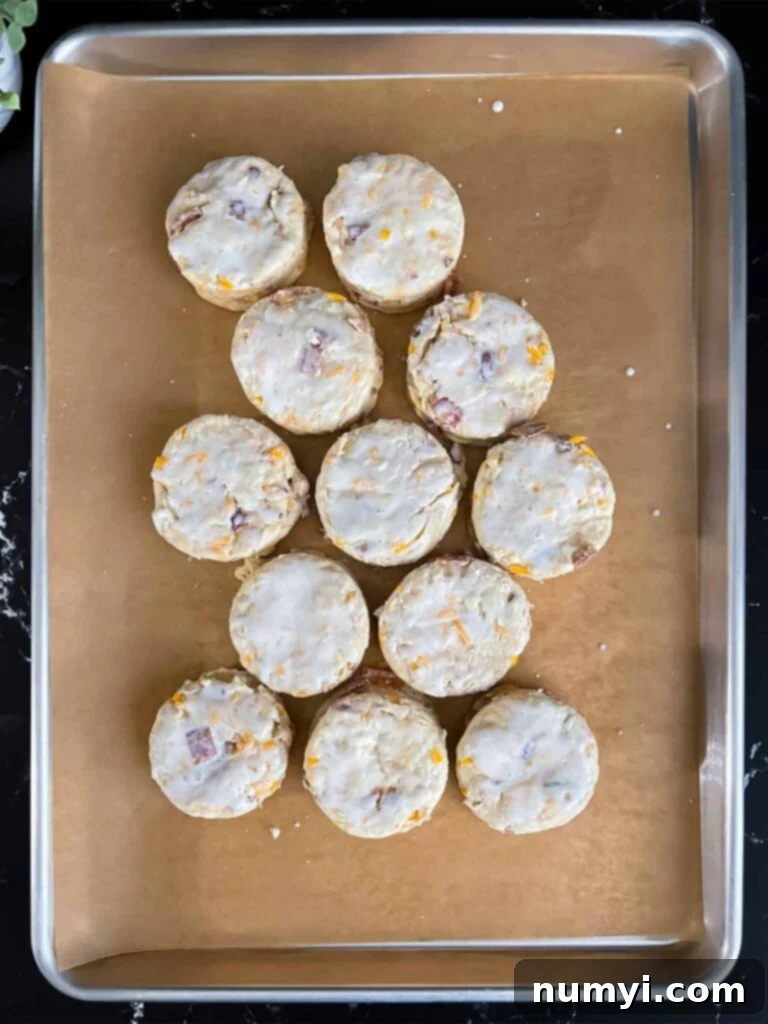 Unbaked bacon cheddar biscuits almost touching on a parchment lined baking sheet.