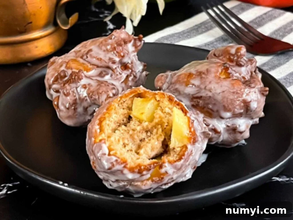 Sweet Apple Puffs 2 Apple fritters on a dark plate on a dark surface.