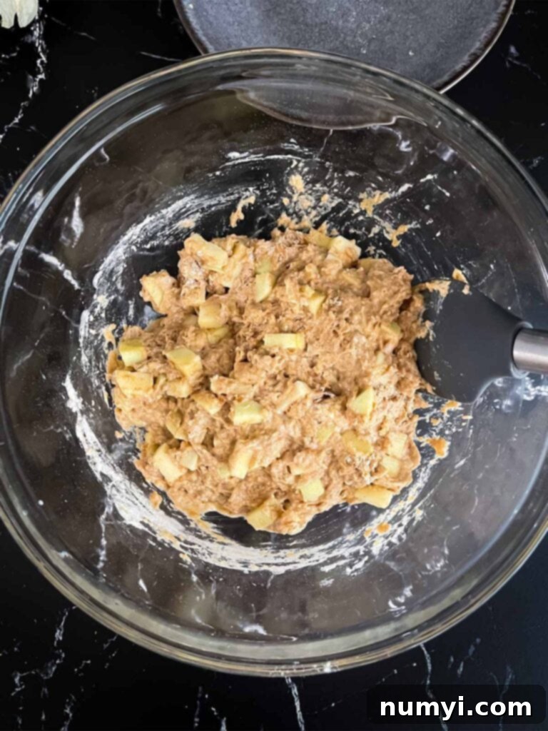 Sweet Apple Puffs 6 Apple fritters batter mixed in a glass mixing bowl on a dark surface.
