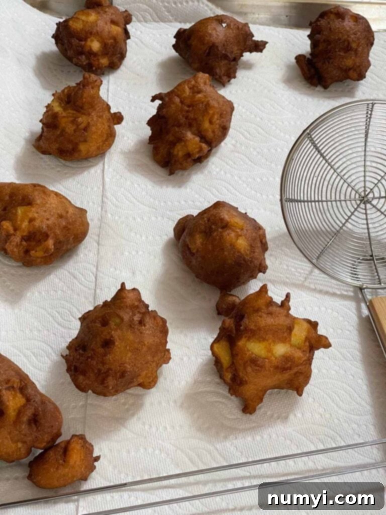Sweet Apple Puffs 8 Fried apple fritters on a paper towel lined baking sheet.