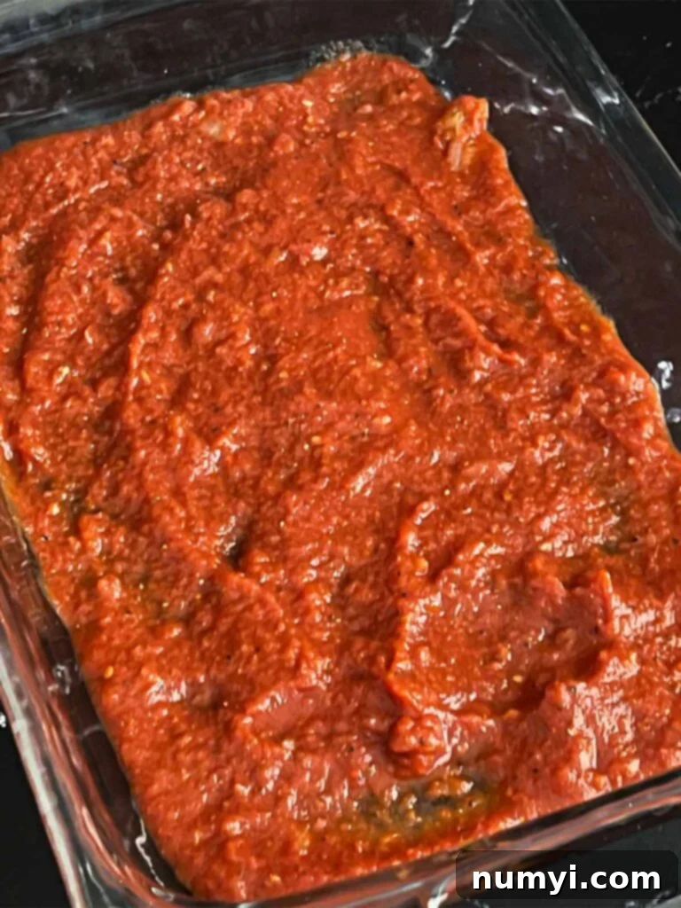 A 9x13 inch casserole dish with a layer of red marinara sauce spread evenly at the bottom.