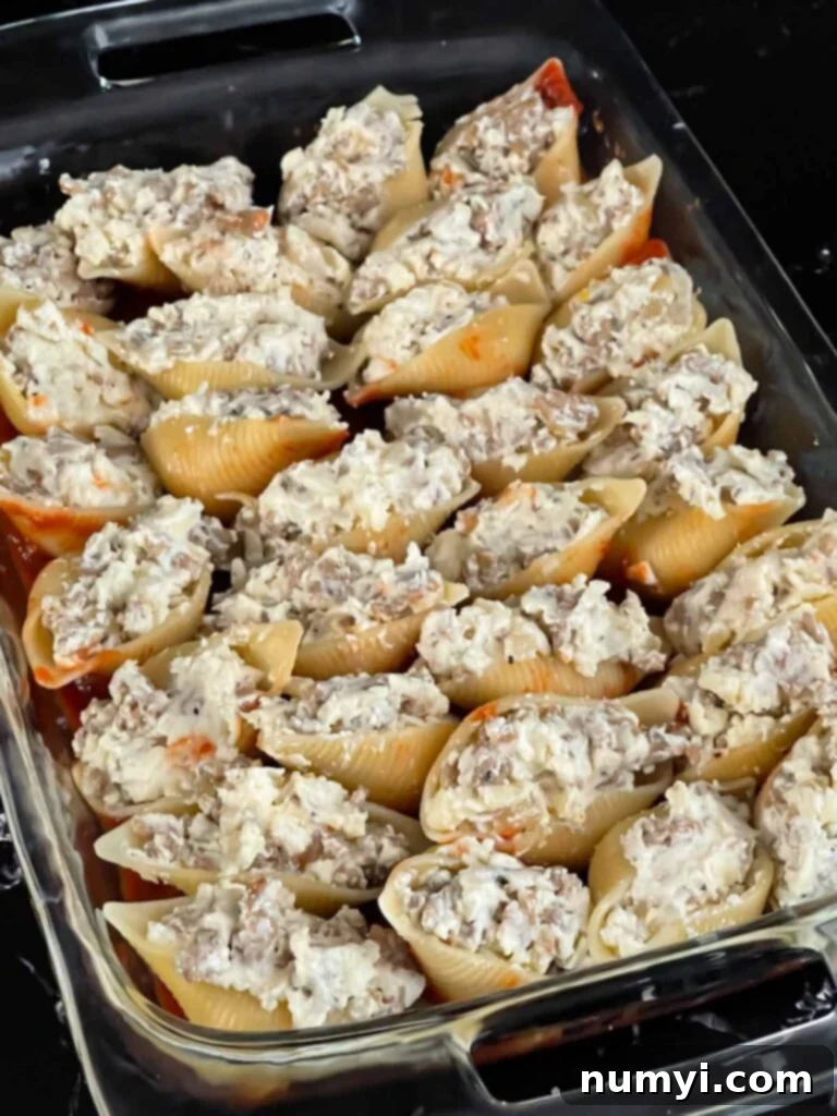 Rows of jumbo pasta shells, neatly stuffed with Italian sausage and cheese, arranged in a marinara-lined casserole dish, ready for the next layer.