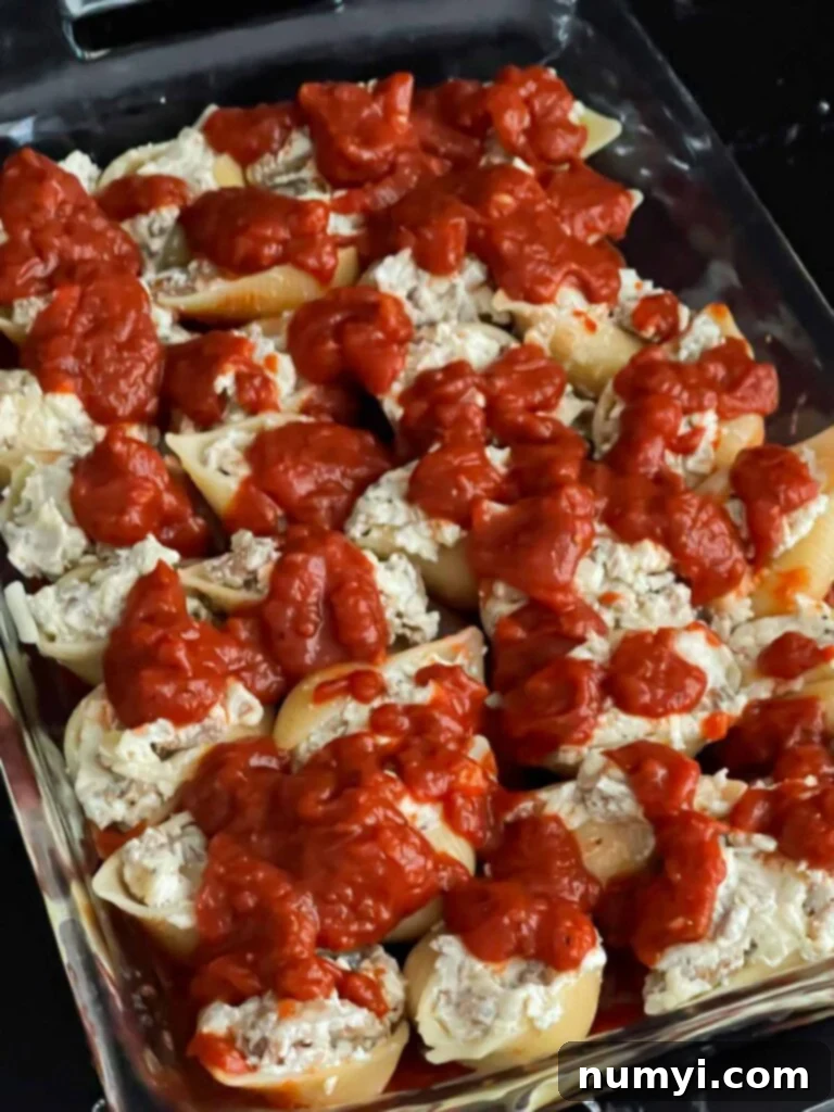 Unbaked Italian sausage stuffed shells in a casserole dish, topped with a rich layer of marinara sauce.