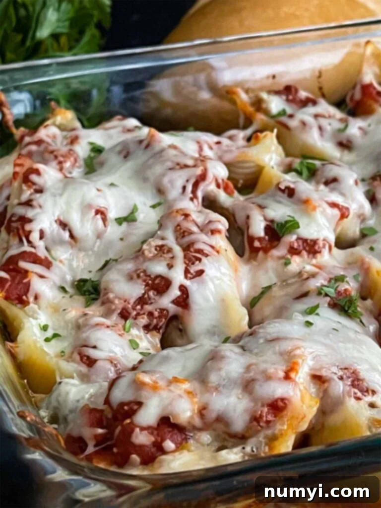 A serving of Italian sausage stuffed shells on a black plate, garnished with fresh herbs, with a casserole dish and bread out of focus in the background.