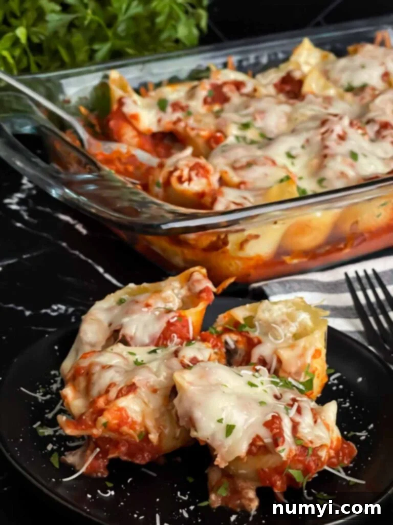 A close-up of baked Italian sausage stuffed shells on a black plate, with a full casserole dish in the background, both showing rich marinara and melted cheese.