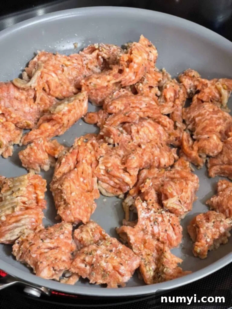 Chopped onions added to browned Italian sausage in a skillet, ready to be cooked further.