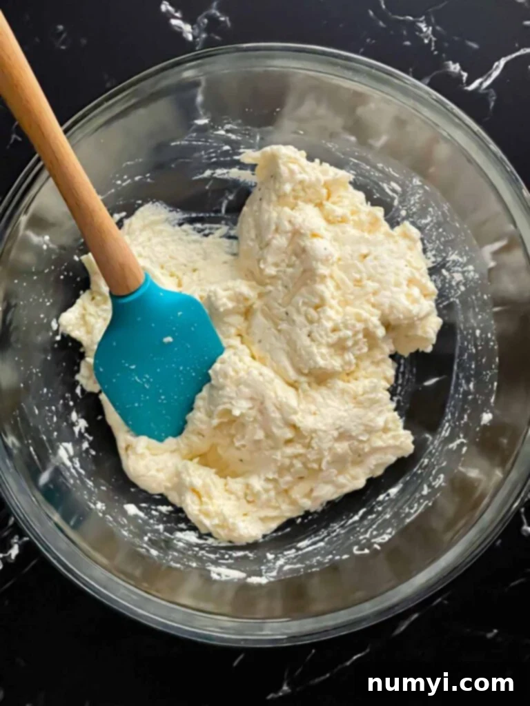 A glass bowl filled with a creamy mixture of ricotta and mozzarella cheese, ready for the sausage.