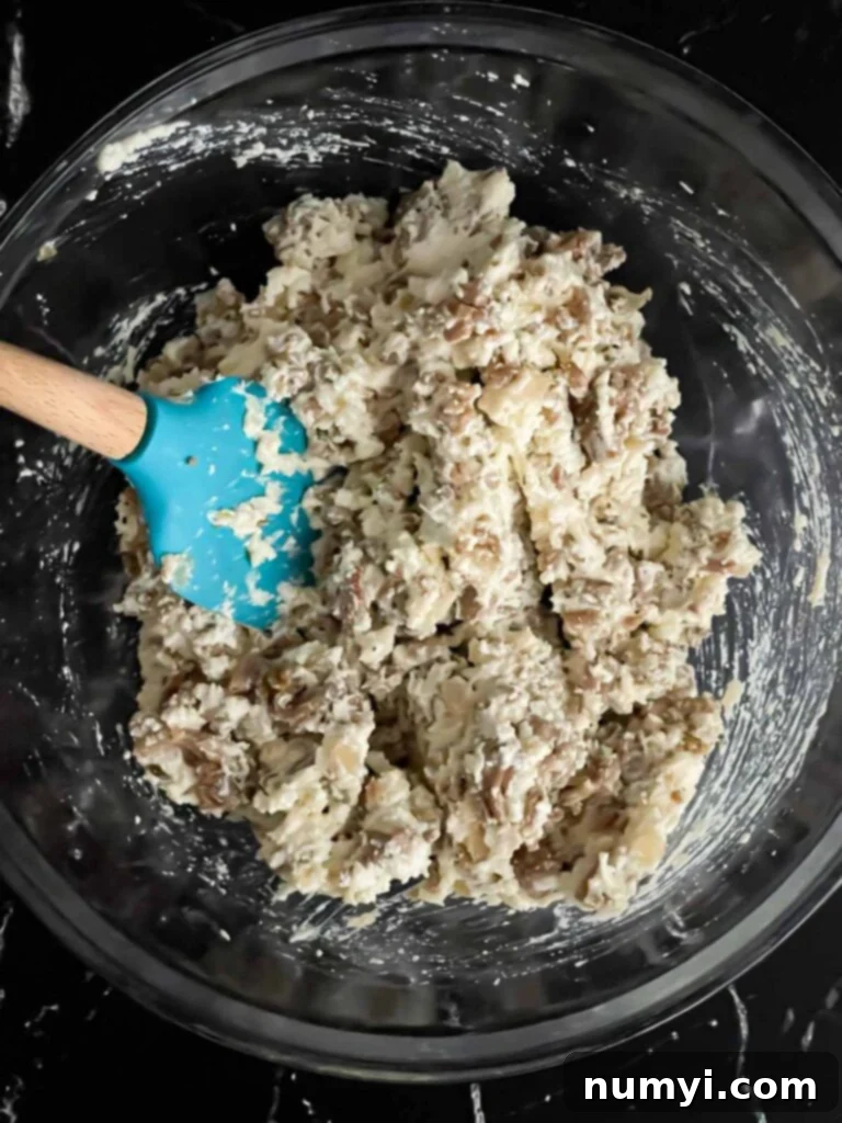 A glass bowl containing the mixed Italian sausage and three-cheese filling, ready for stuffing the pasta shells.