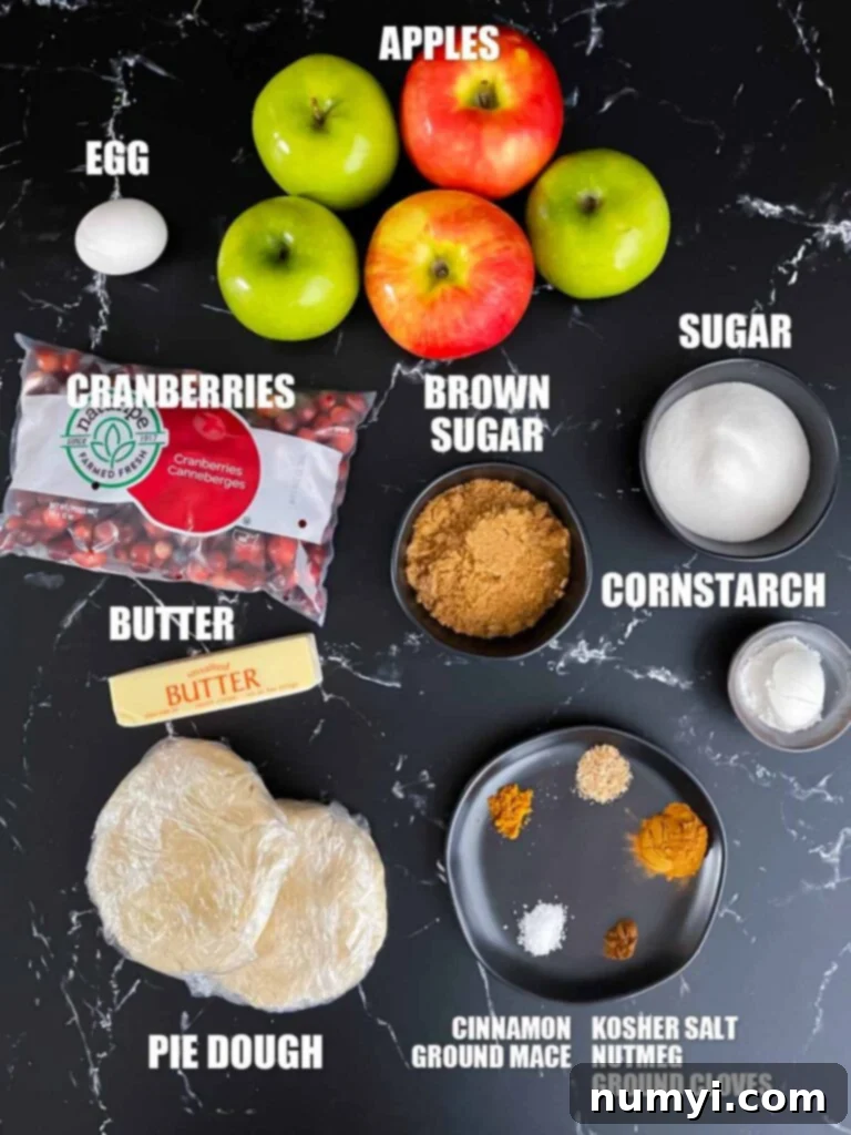 Various ingredients for the cranberry apple pie recipe, including apples, cranberries, sugar, and spices, arranged neatly on a dark surface.