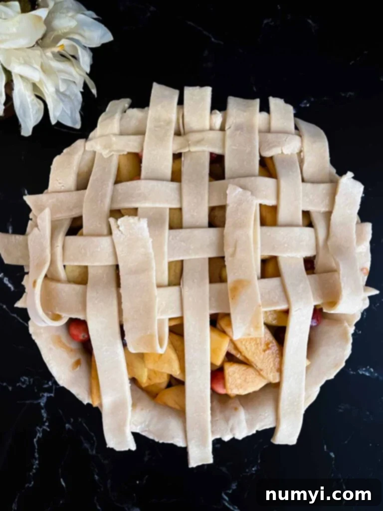 A beautifully woven lattice pie crust sitting atop the vibrant cranberry apple pie filling, ready for baking.