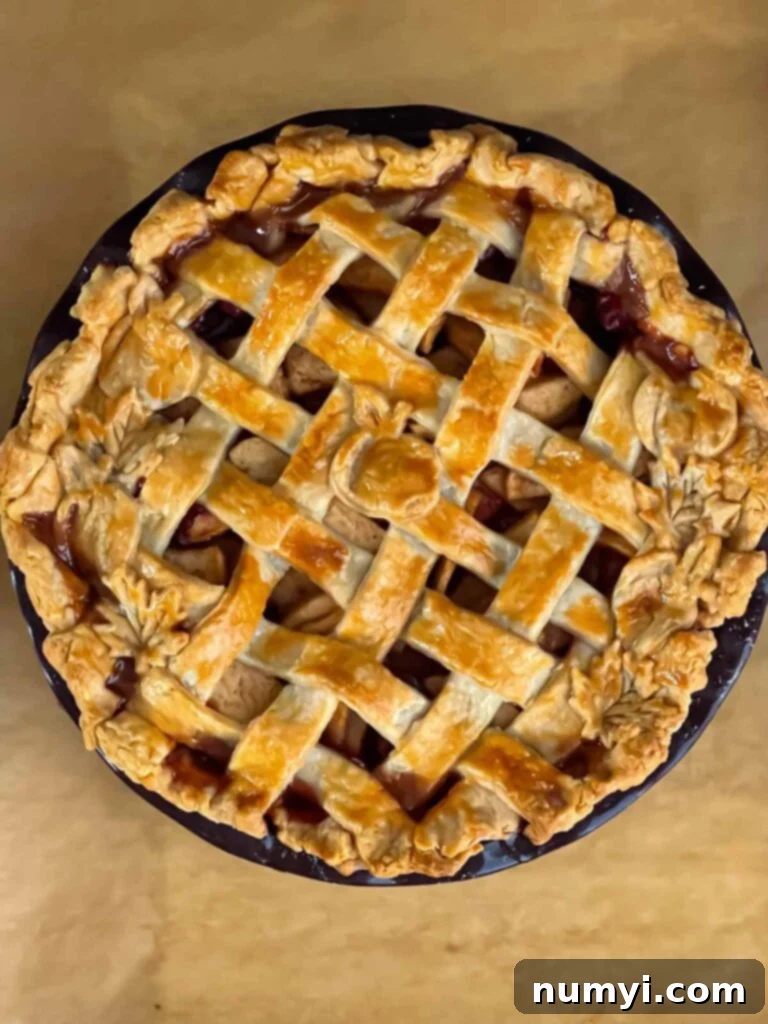A perfectly golden-brown baked cranberry apple pie on a parchment paper-lined baking sheet, showing off its beautiful lattice crust.