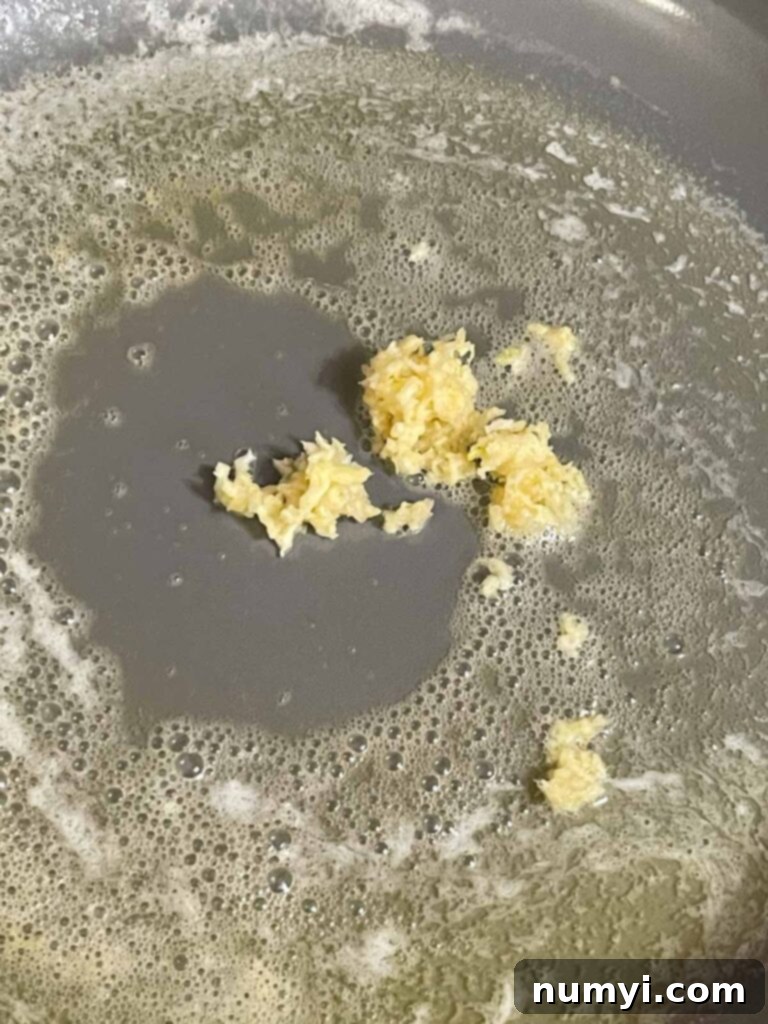 Adding garlic to butter in a skillet for Alfredo sauce.