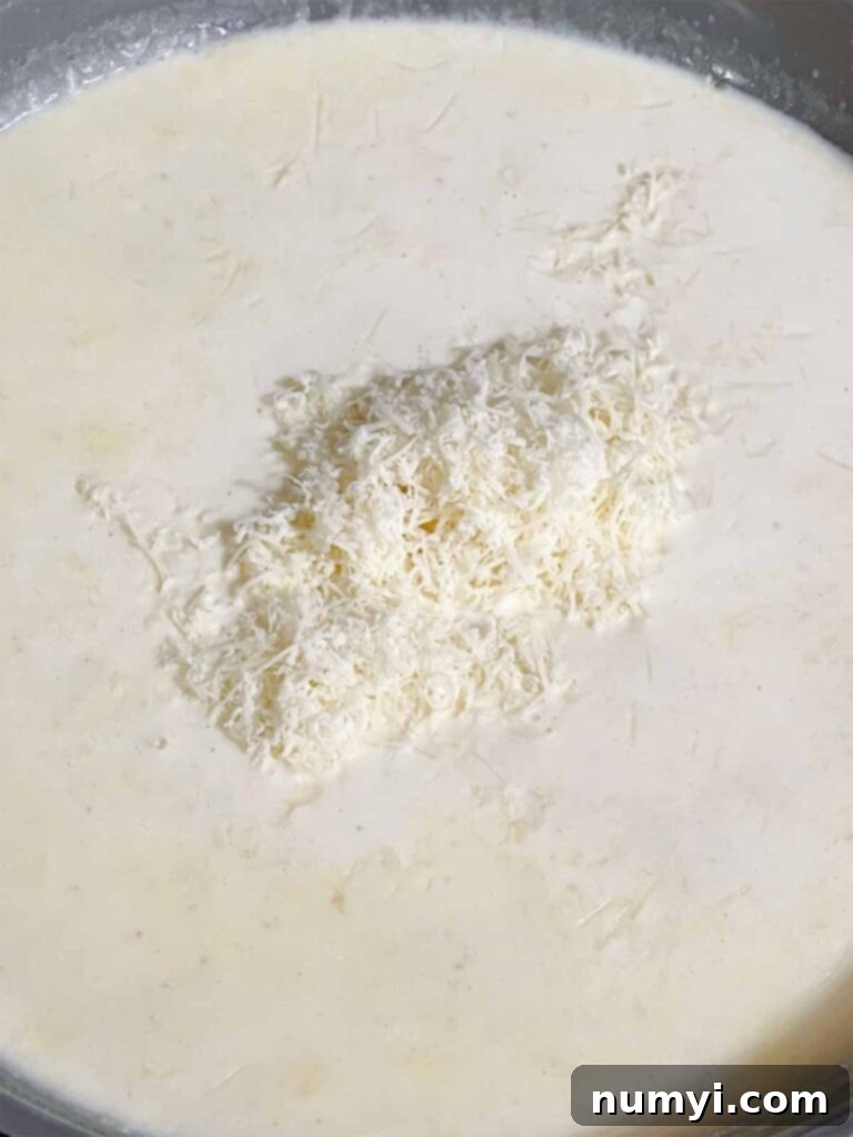 Adding parmesan cheese to a creamy Alfredo sauce.
