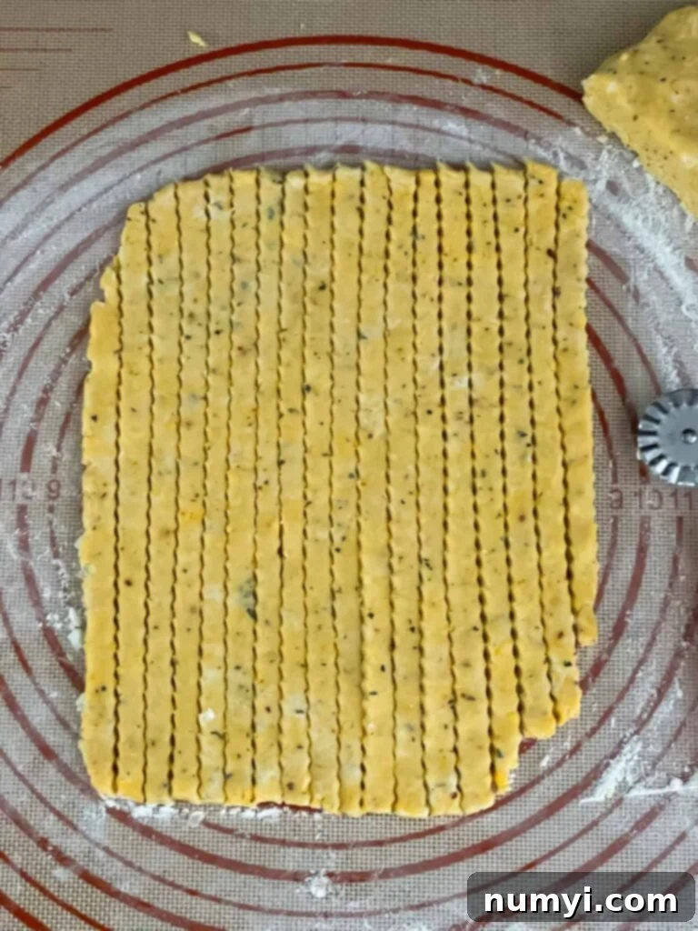 Crispy Cheddar Herb Sticks 11 Cheddar and herb dough expertly cut into thin, uniform straws on a dough mat, ready for transfer to the baking sheet.