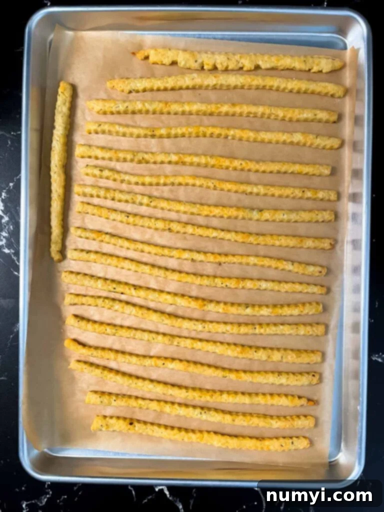 Crispy Cheddar Herb Sticks 13 Freshly baked golden-brown cheddar cheese and herb straws cooling on a baking sheet, showcasing their crispy perfection.
