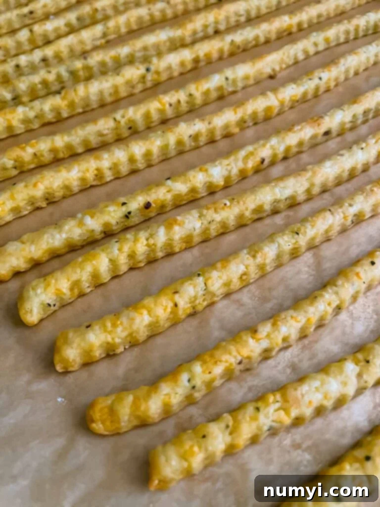Crispy Cheddar Herb Sticks 14 Another perspective of baked cheddar cheese and herb straws, still on the baking sheet, with their delicate texture and golden hue highlighted.