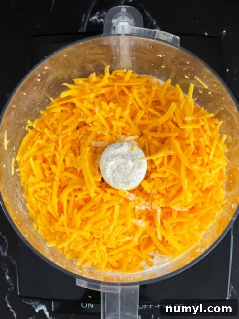 Crispy Cheddar Herb Sticks 4 Close-up of shredded cheddar cheese, fluffy and ready for the next step, inside a food processor bowl.