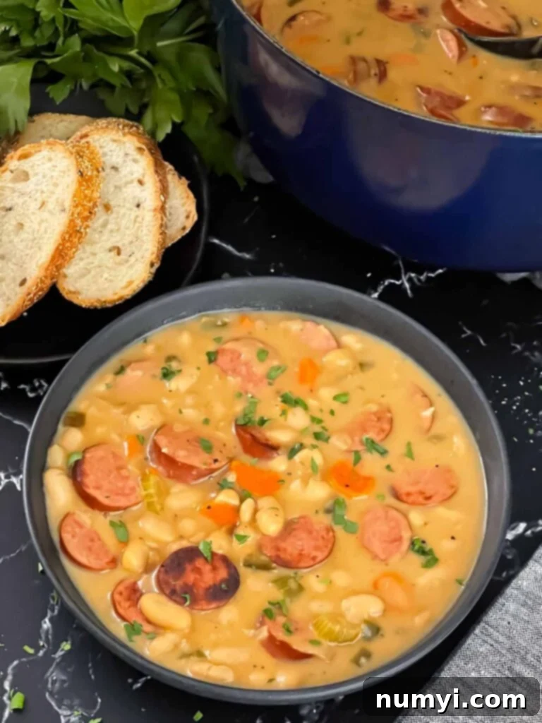 A beautifully presented bowl of creamy bean soup with smoked sausage, bread, and parsley in the background, ready to be enjoyed.