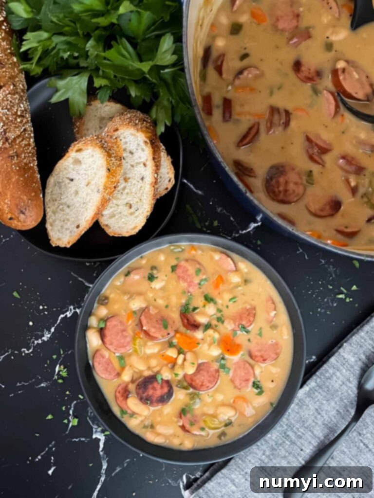 A close-up shot of creamy bean soup with smoked sausage in a bowl, showcasing its rich texture and appetizing ingredients, with bread and parsley in the background.