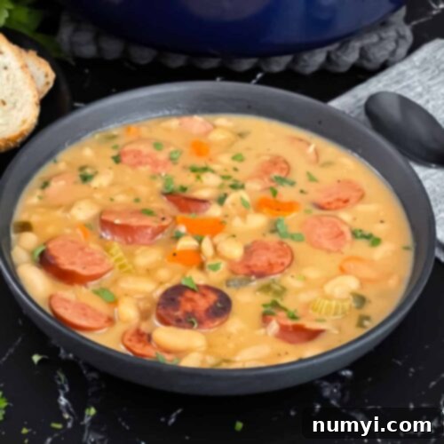 A heartwarming bowl of creamy bean soup with smoked sausage, served with crusty bread and fresh parsley.