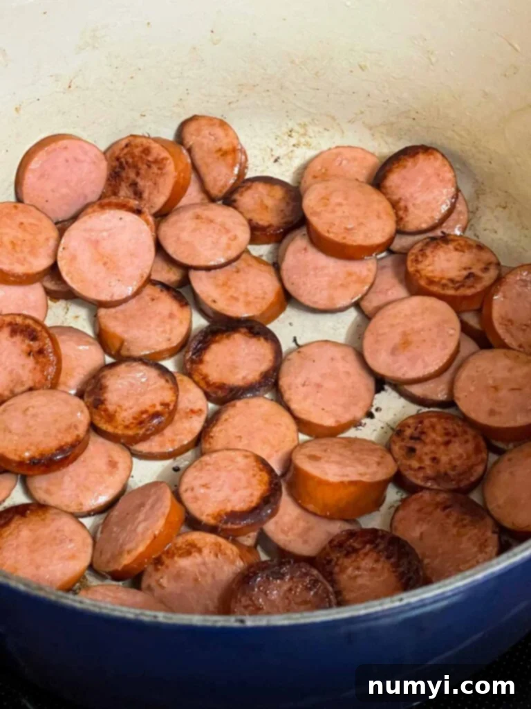 Sliced smoked sausage being browned in a large Dutch oven with vegetable oil.