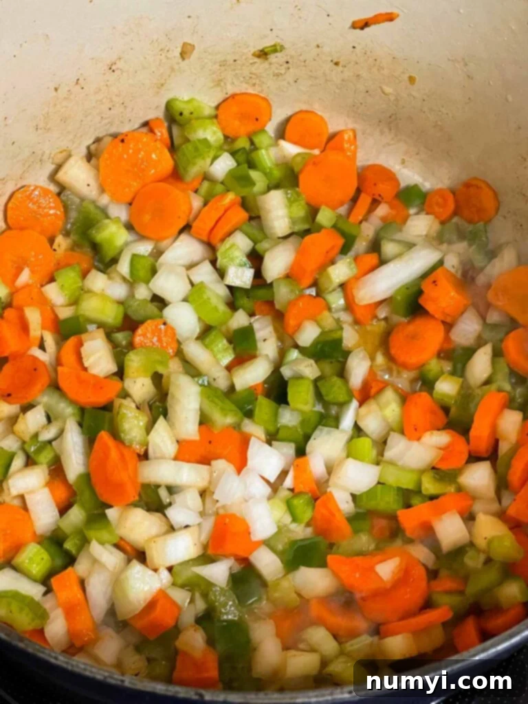 Diced onions, carrots, celery, and green bell pepper sweating in melted butter in a Dutch oven.