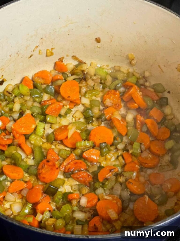 Sautéed vegetables, including cooked onions and tender carrots, in a Dutch oven, releasing their aromas.