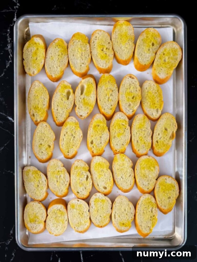 Creamy Baked Ricotta 4 Baguette slices coated with olive oil laid out on a parchment-lined baking sheet, ready for toasting.