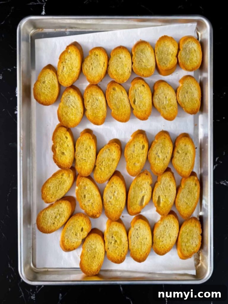 Creamy Baked Ricotta 5 Golden brown, perfectly toasted baguette slices on a parchment-lined baking sheet, glistening with olive oil.