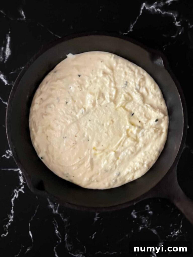 Creamy Baked Ricotta 8 Creamy ricotta dip mixture spread evenly in a cast iron skillet, ready for the cheese topping.