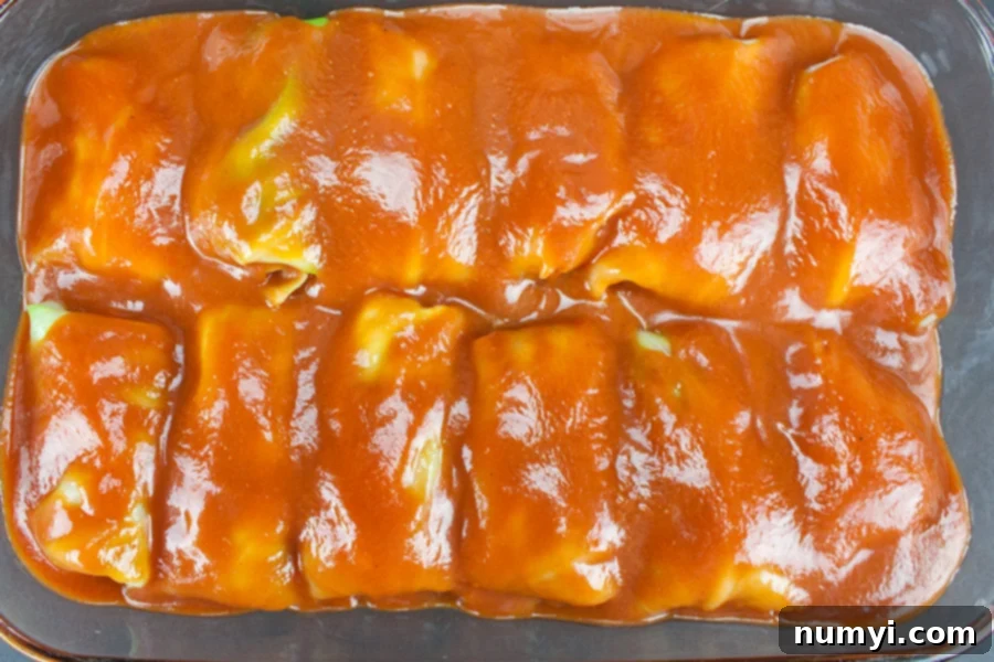 Unbaked cabbage rolls nestled in a glass baking dish, completely covered in the rich tomato sauce, ready for the oven.