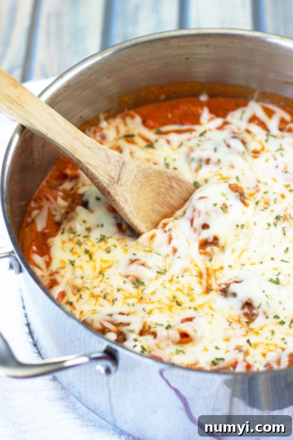 A large, rustic pot filled with bubbling creamy marinara meatballs and penne pasta, topped with melted mozzarella cheese and a large wooden spoon resting inside, ready to serve.