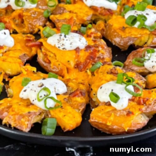 Loaded smashed potatoes on a black serving plate.