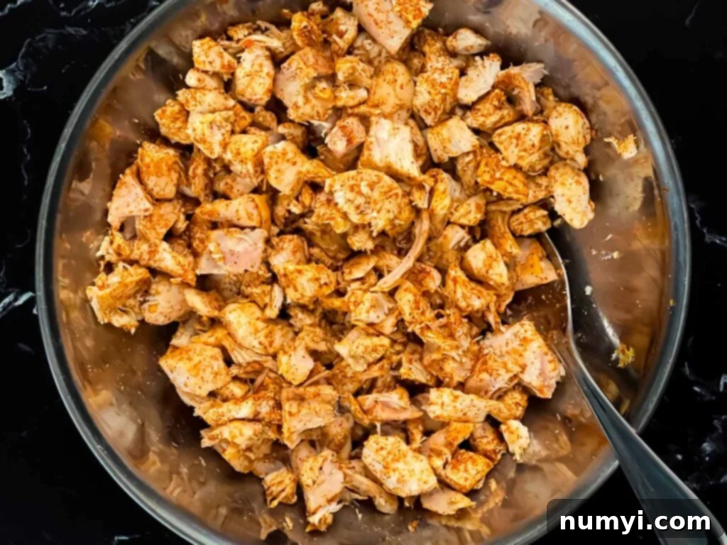 Cooked seasoned chicken in a stainless steel bowl, ready for mixing.
