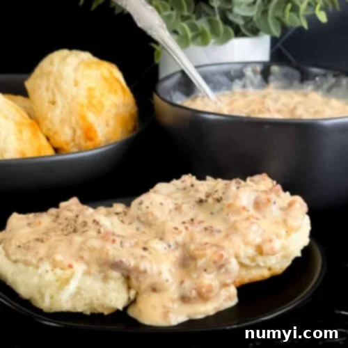 Effortless Country Sausage Gravy 10 Biscuits and sausage gravy on a black plate.