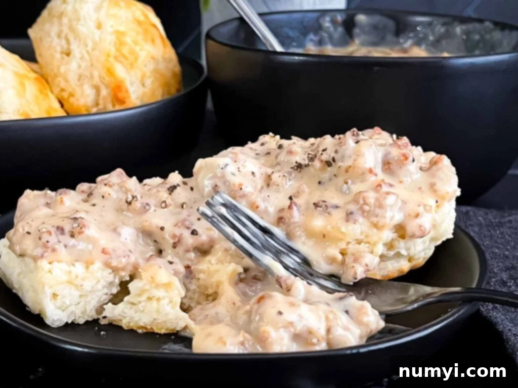 Effortless Country Sausage Gravy 3 Biscuits and sausage gravy on a black plate.