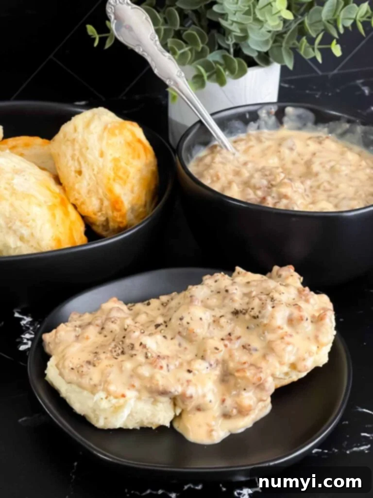 Effortless Country Sausage Gravy 9 Biscuits and sausage gravy on a black plate.